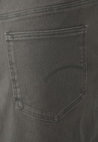 Svarte denimjeans har en baklomme med en subtil buet sømdetalj. Stoffet har en glatt, teksturert finish.
