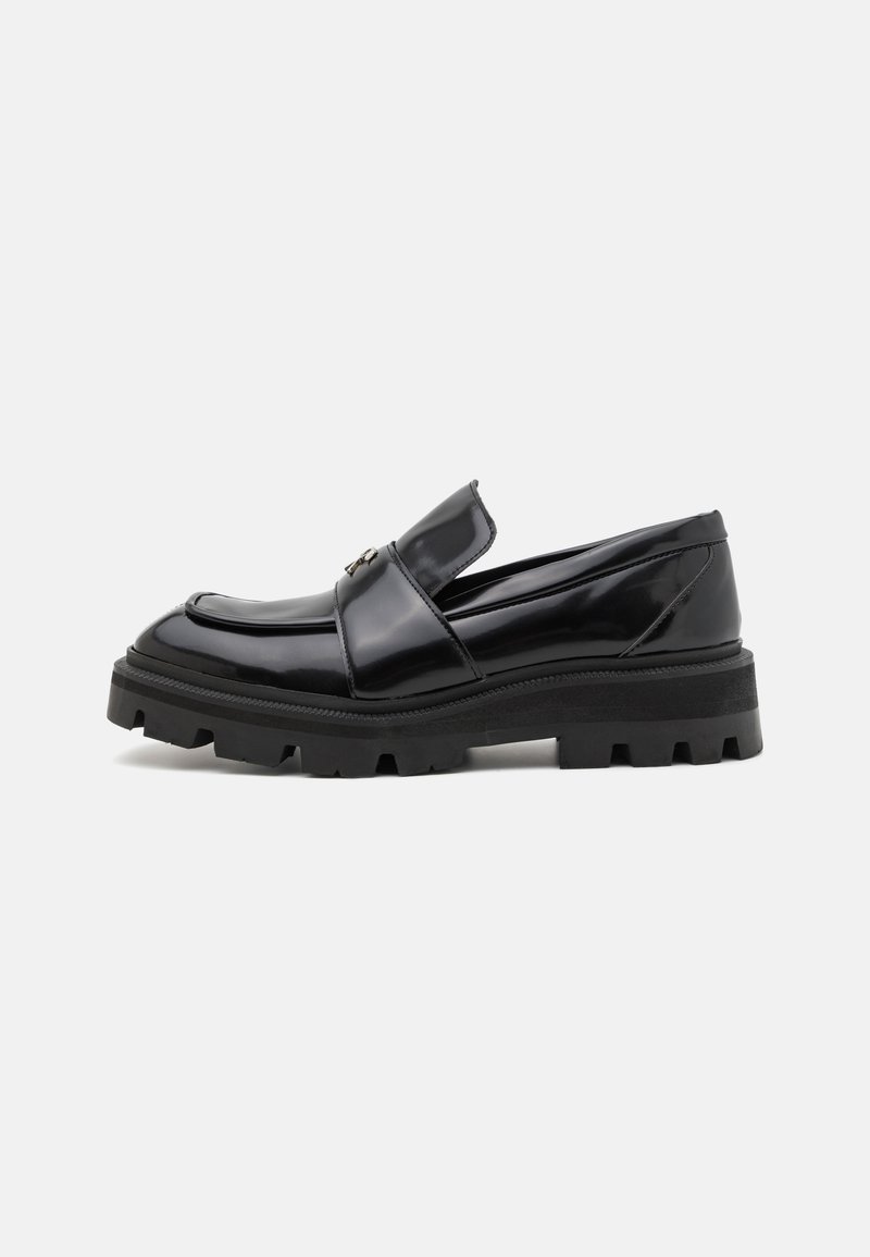 Black polished leather loafers with a wide strap and decorative hardware, featuring a thick, textured rubber sole for added grip.