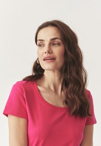 Kortærmet T-shirt i lys pink bomuld med rund halsudskæring, glat tekstur og enkel design. Ingen mønstre eller hardware synlige.