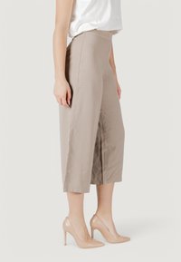 Pantalones cortos beige con cintura alta, hechos de una tela suave, que cuentan con aberturas laterales y se combinan con zapatos de tacón nude.