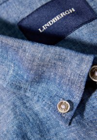 Denim overhemd in een lichtblauwe kleur, zachte textuur, knoopdetails en een donkerblauwe label met de merknaam "Lindbergh."