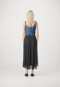 Denim kratka majica s tankimi naramnicami in detajlom v obliki loka, v kombinaciji z dolgim, nabranim črnim krilom in črnimi salonarji z visoko peto.