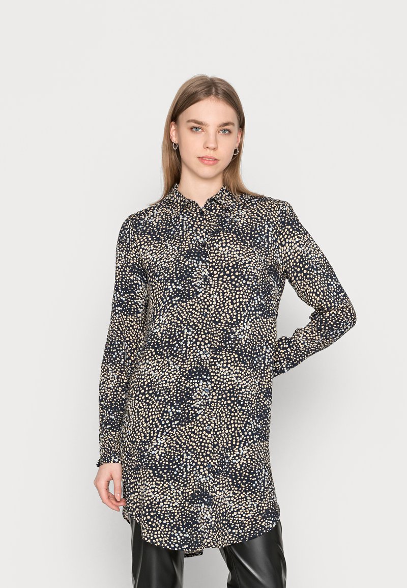 Camicia a maniche lunghe di un blu navy scuro con un leggero motivo a pois, dotata di un colletto e di una linea dritta. Tessuto dalla consistenza liscia.