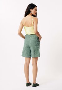 Groen gestreepte shorts van stof, gecombineerd met een lichtgele tanktop. De shorts hebben zijzakken en een relaxte pasvorm.