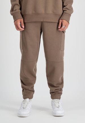 Pantalones de chándal marrones con un corte relajado, puños elásticos, bolsillos laterales y cinturilla acanalada. Combinados con zapatillas blancas.