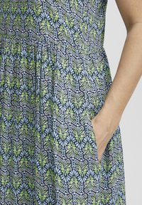Robe à motif floral bleu marine avec des accents verts et bleu clair, présentant une taille cintrée, un tissu fluide et des poches latérales.