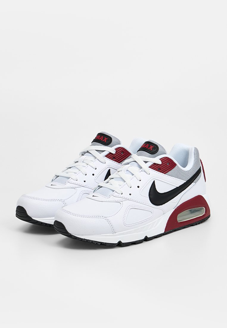 Paire de baskets blanches Nike Air Max avec un swoosh noir, des accents rouges et un coussin d’air visible sur fond blanc.
