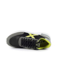 Baskets noires et grises avec un dessus texturé, des accents jaunes et des lacets noirs. Présente une semelle blanche et un logo sur le côté.