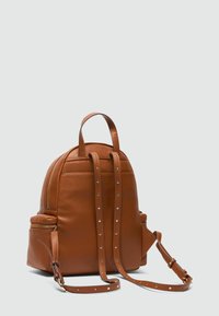 Sac à dos en cuir marron offrant une forme arrondie, deux poignées supérieures, des bretelles réglables et des clous dorés le long des bretelles et de la fermeture éclair.