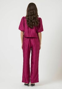 Magenta kahden osan asu, joka koostuu lyhythihaisesta topista, jossa on pörhöhihoja, ja leveälahkeista housuista, molemmissa on kohokuvioinen aaltoilu.