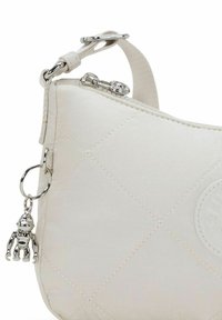 Quilted lys creme håndtaske med en sølvhardware nøglering charm, der har en rund form og en struktureret overflade, sikret med en lynlås.