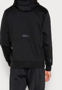 Sudadera con capucha negra hecha de felpa. Presenta un logo en la parte trasera y acentos triangulares azules en los puños. Diseño simple, corte holgado.