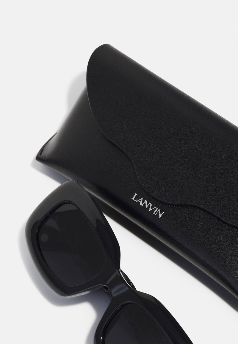 Black rectangular sunglasses with dark lenses beside a black leather case featuring a curved flap and embossed "LANVIN" logo.