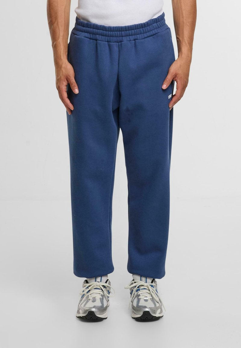 Blauwe sweats met een elastische tailleband en zijzakken, gemaakt van zachte stof, gecombineerd met grijze en witte sportschoenen.
