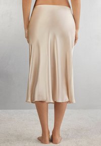 Jupe midi en satin beige avec une texture lisse, une silhouette fluide et une taille élastique, atteignant juste en dessous du genou.