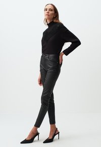 Maglione nero a costine con dettaglio decorativo in crochet sul collo, abbinato a pantaloni in pelle neri aderenti e décolleté neri a punta.