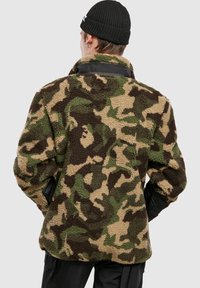 Fliisist jakk kamuflaažimustris, millel on roheline, pruun ja beež värv. Tekstuuriga kangas, mustad detailid ja krae disain.