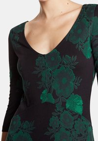 Robe noire avec un profond décolleté en V et des manches trois-quarts. Décorée de motifs floraux vert foncé et en tissu de coton lisse.