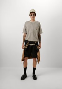 Striped beige t-shirt with a round neckline, black shorts, a beige beanie, and round sunglasses. Black shoes with tassels complete the look.