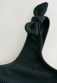 Fekete, textúrált szövet, csomózott masni részlettel a pánton. Az anyag bordázott mintázatú, ami tapintható felületet kölcsönöz.