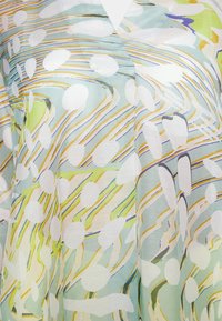 Leichte, transparente Bluse in Pastellfarben mit abstrakten Wirbeln, weißen Punkten und gelben Akzenten auf einem blau-grünen Hintergrund.