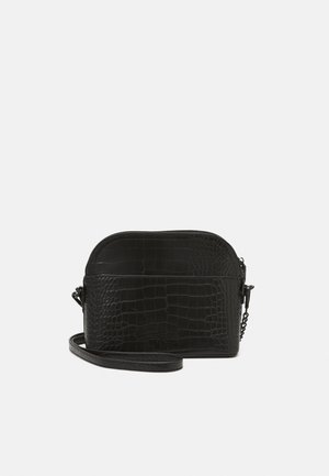 Sac bandoulière en similicuir noir à texture crocodile, fermeture éclair et sangle amovible. Présente un dessus arrondi et un branding discret.