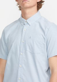 Chemise à manches courtes, bleu clair, en tissu doux, avec une poche poitrine unique et un petit logo brodé.