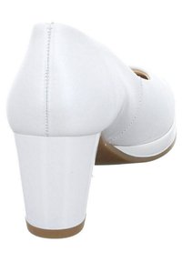 Chaussure blanche à talon haut avec une tige en cuir lisse, un bout rond et un talon bloc. La semelle est marron clair avec une légère courbure à l'avant.