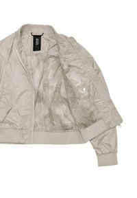 Bomber jacket color beige chiaro realizzato in un tessuto liscio e lucido. Presenta una chiusura con zip, polsini elasticizzati e una fodera interna decorata con etichette impermeabili.