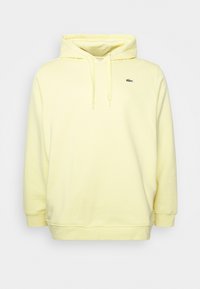 Gul huvtröja med känguruficka, justerbara snoddar och en liten grön krokodil-logotyp på vänster bröst.