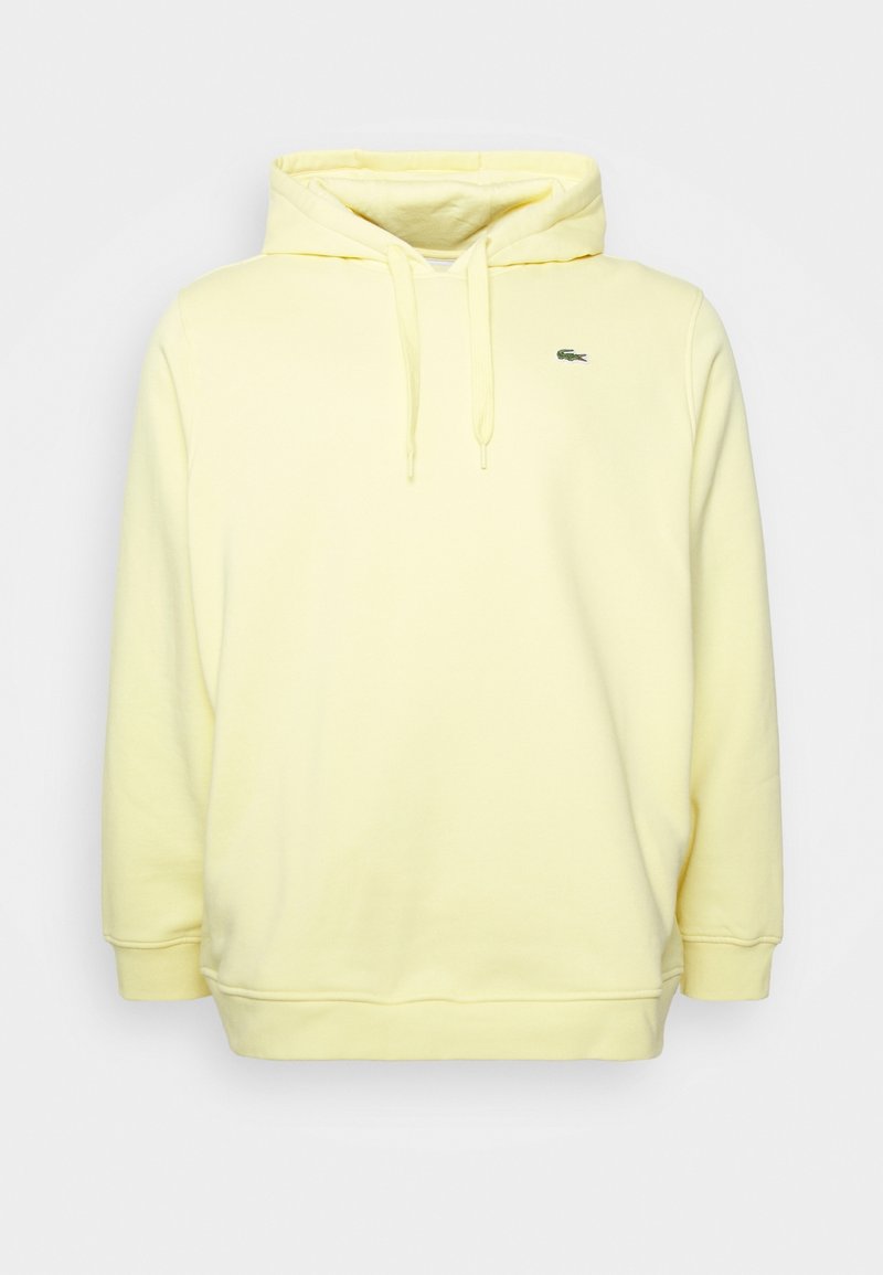 Gul huvtröja med känguruficka, justerbara snoddar och en liten grön krokodil-logotyp på vänster bröst.