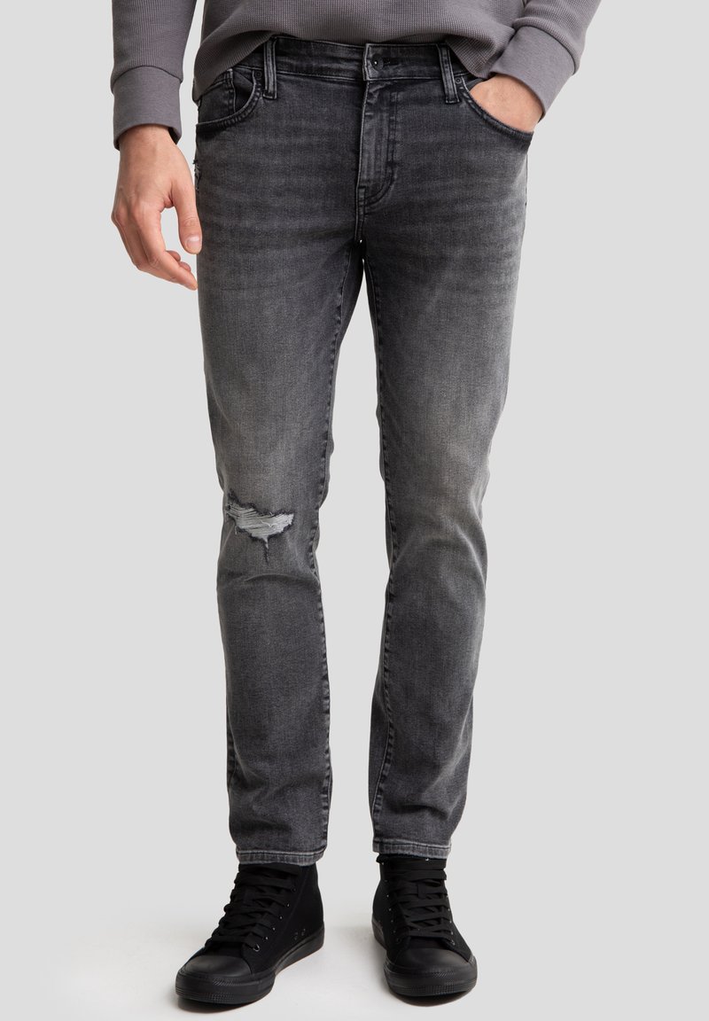 Jeans de mezclilla gris con un corte ajustado, que presentan un detalle desgastado en la rodilla, diseño de cinco bolsillos y rematados con un cinturón negro. Combinados con zapatillas negras.