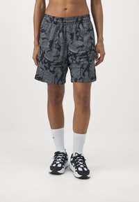 Shorts à motifs noirs et blancs avec une taille à cordon, longueur au-dessus du genou, associés à des chaussures de sport noires et blanches et des chaussettes blanches.