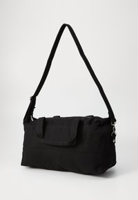 Bolsa de deporte de tela negra con correa de hombro desmontable, dos asas en la parte superior, base plana y cierre con cremallera. Presenta acentos de hardware en color plateado.