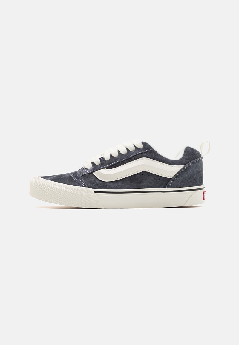 Zapatillas de ante en azul marino con detalles en blanco, punta redonda y diseño de cordones. Presenta una superficie texturizada y una suela de goma, con una marca en el talón.