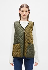 Γιλέκο με ραφή κουβερτούλα σε ελιά και μουσταρδί, με κλείσιμο με φερμουάρ, στρογγυλή τράβηγμα δακτυλίου και δύο μπροστινές τσέπες. Διαθέτει λεπτομέρειες με αντίθετη τρέσα.