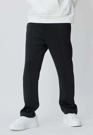 Pantalon noir sur mesure à jambes droites, en tissu doux, avec détail de couture latérale et coupe confortable, assorti à des baskets blanches.