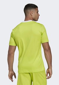 Neon gul athletic jersey med korte ærmer, hvit krage, glatt tekstur og løs passform, vist fra baksiden med matchende shorts.