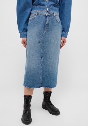 Denim rok met een middellang ontwerp, voorzien van een voornaad en een rechte silhouet. Draagt met zwarte veterschoenen.