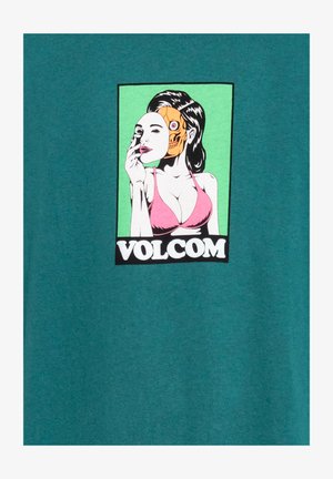 T-shirt in cotone teal con una grafica di una donna con metà faccia da scheletro. Il design include colori vivaci con un bikini rosa e uno sfondo verde.