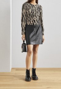 T-shirt à manches longues avec un motif zébré beige et noir, associé à une jupe en cuir noire et des bottes à lacets noires. Petit sac noir.
