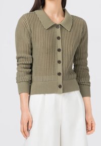 Olivgrön stickad cardigan med krage, med knäppning framtill och ribbade ärmavslut. Texturen är lös stickad med en figurnära nederkant.