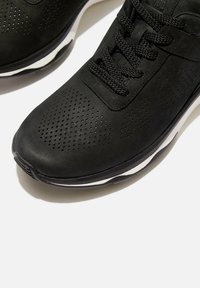 Zwarte sportschoenen van geperforeerd materiaal met een gestructureerde afwerking, voorzien van platte zwarte veters en een contrasterende witte zool.