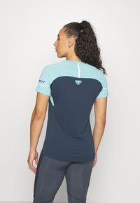 Κοντομάνικο αθλητικό μπλουζάκι με ελαφρύ μπλε πάνω τμήμα και σκούρο μπλε κάτω τμήμα, εφαρμοστή γραμμή και μινιμαλιστικό λογότυπο κοντά στον λαιμό.