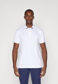 Hvit polo skjorte med korte ermer, en flat krage med svarte striper, og en knappestolpe. Glatt tekstur, tettsittende design.