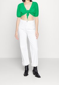 Haut vert court à manches bouffantes avec fermeture à nouer, associé à un jean blanc taille haute et des bottines à talons noires.