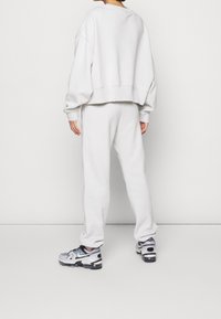 Ljust grå bomullströja med sänkt axel, parat med matchande sweatpants. Märkbar textur och en avslappnad passform. Skorna har svarta accenter.