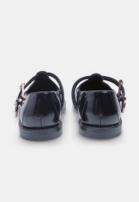 Sandalias negras de charol con la parte trasera abierta, que cuentan con correas delgadas, cierre de hebilla y suela plana. Textura lisa y brillante en toda su superficie.