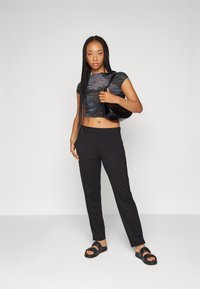 Svart cropped topp med teksturert design, kombinert med svarte skreddersydde bukser og svarte sandaler. Modellen holder en svart skulderveske.