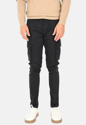 Pantaloni cargo neri con vestibilità slim, dotati di tasche laterali, realizzati in tessuto resistente, abbinati a sneakers bianche e un maglione beige.